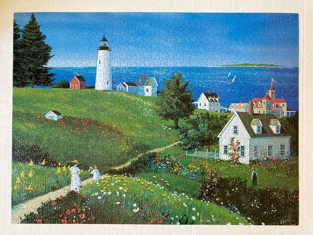A peaceful coastal landscape featuring a white lighthouse, several cottages, and people strolling through a flower garden.