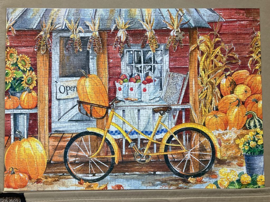 A bright yellow bicycle stands in front of a rustic red barn decorated with autumn pumpkins, corn, and sunflowers.