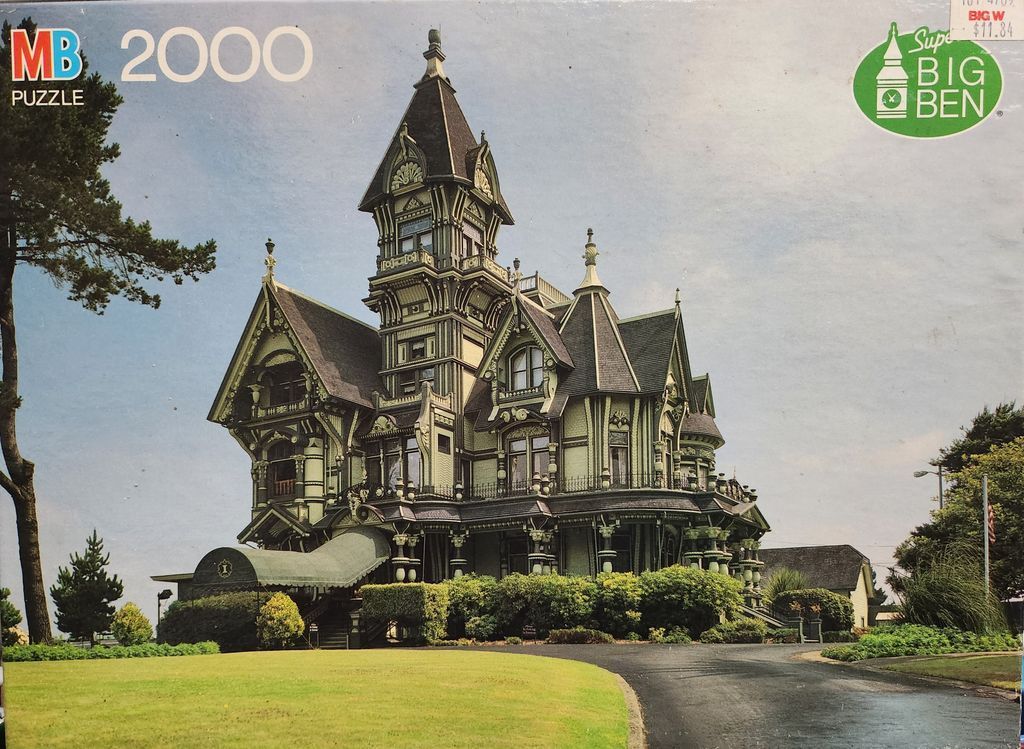 A detailed photograph of a large, ornate Victorian-style mansion with complex woodwork and a tall central tower.