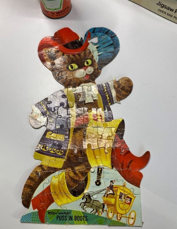 A die-cut vintage-style illustration of Puss in Boots wearing a feathered hat and cape.