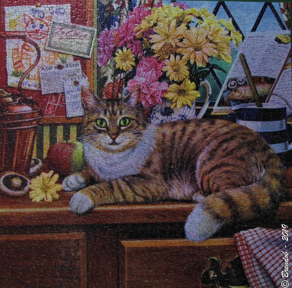 A tabby cat resting on a rustic wooden table surrounded by kitchen items and flowers.