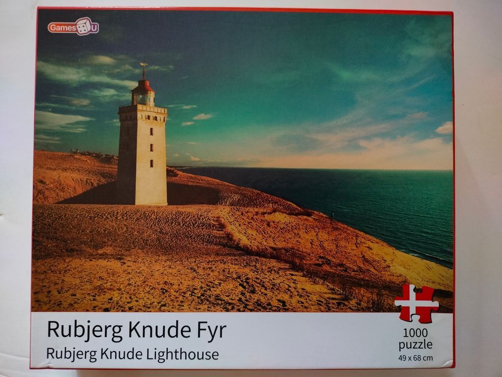A photograph of Rubjerg Knude lighthouse standing on a sandy cliff overlooking the sea under a dramatic teal sky.