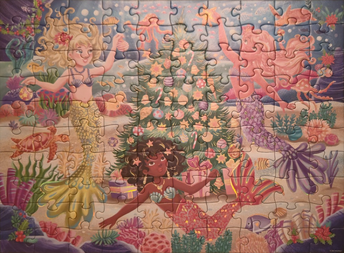 Three mermaids decorating an underwater Christmas tree surrounded by coral and sea life.