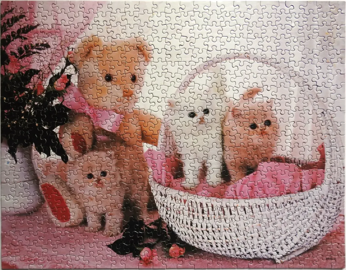 A teddy bear sitting next to a white basket containing two fluffy kittens against a soft pink background.