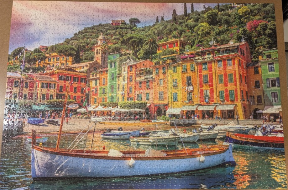 A vibrant Mediterranean harbor scene featuring colorful buildings and a light blue wooden boat in the foreground.