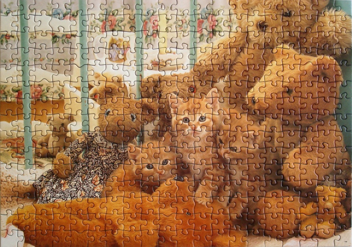 A group of teddy bears and kittens huddled together behind a wooden crib railing.