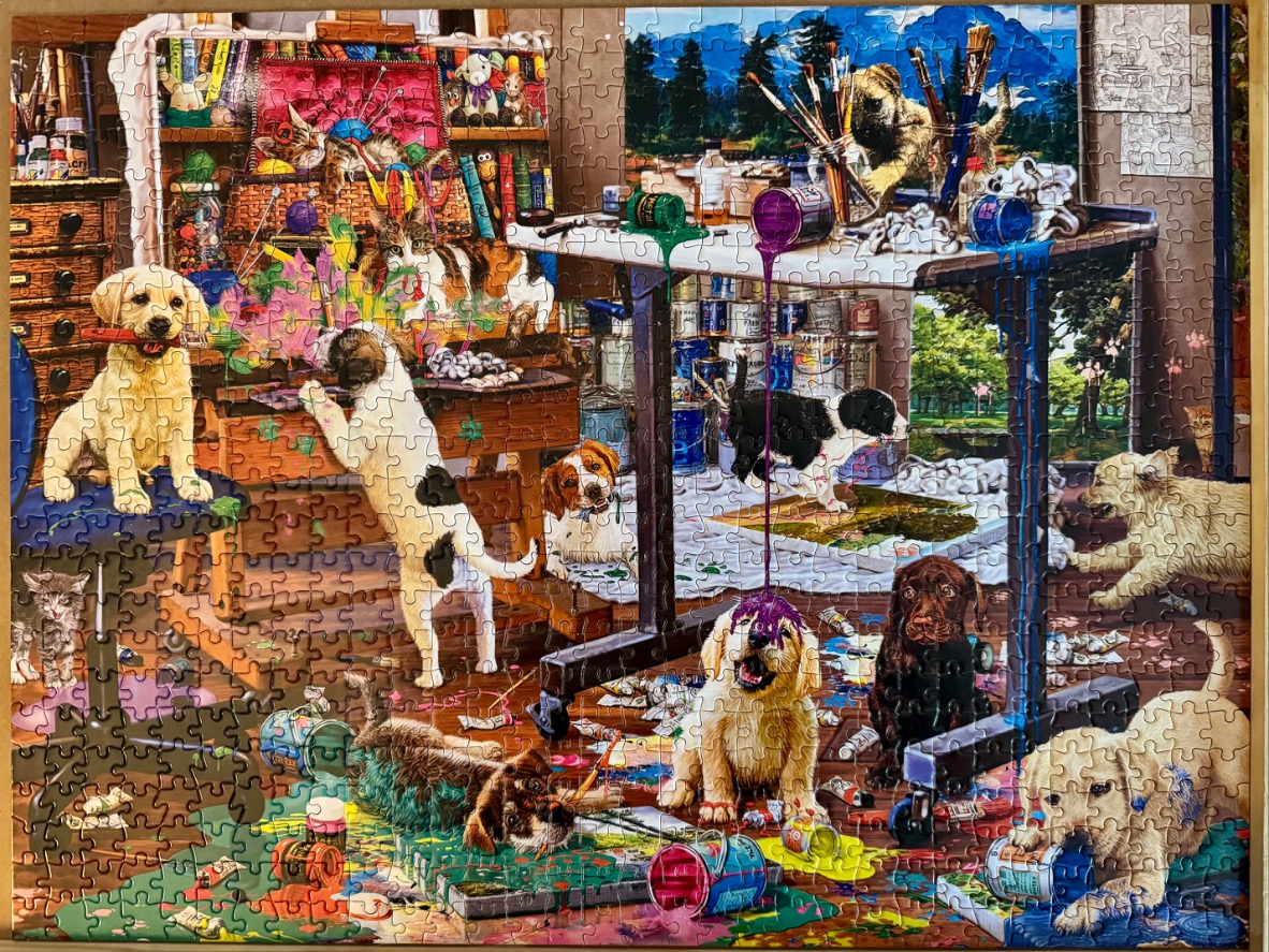A chaotic art studio filled with many playful puppies covered in colorful paint.