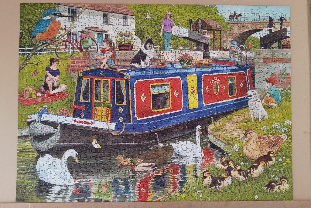 A colorful narrowboat docked on a canal with people, dogs, ducks, and swans.