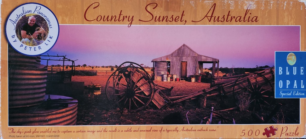 A photograph of an Australian outback farmstead under a pink sunset sky featuring a rusted wooden cart and a metal shed.