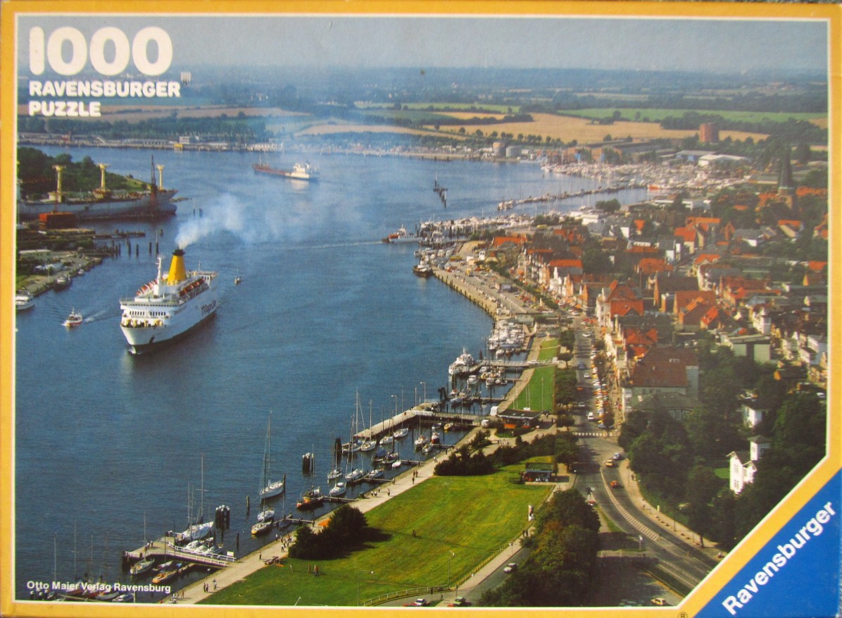 Aerial view of a German seaside town with a large cruise ship in a deep blue harbor.