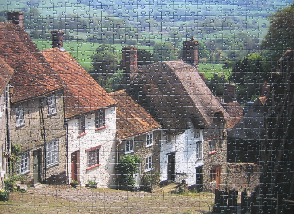 A row of traditional English stone cottages with red tiled and thatched roofs overlooking a green valley.