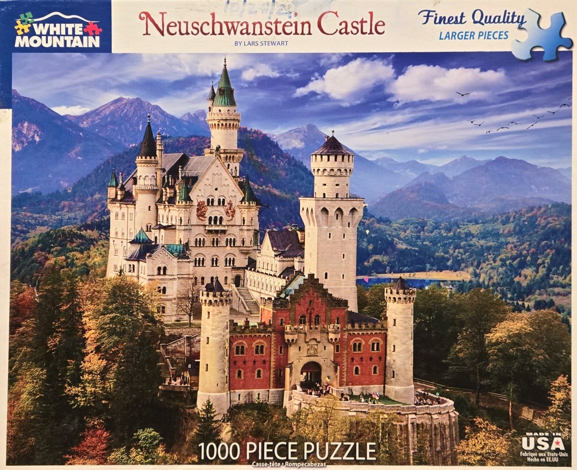 Neuschwanstein Castle in Bavaria, Germany, surrounded by autumnal forests and distant mountains under a blue sky.