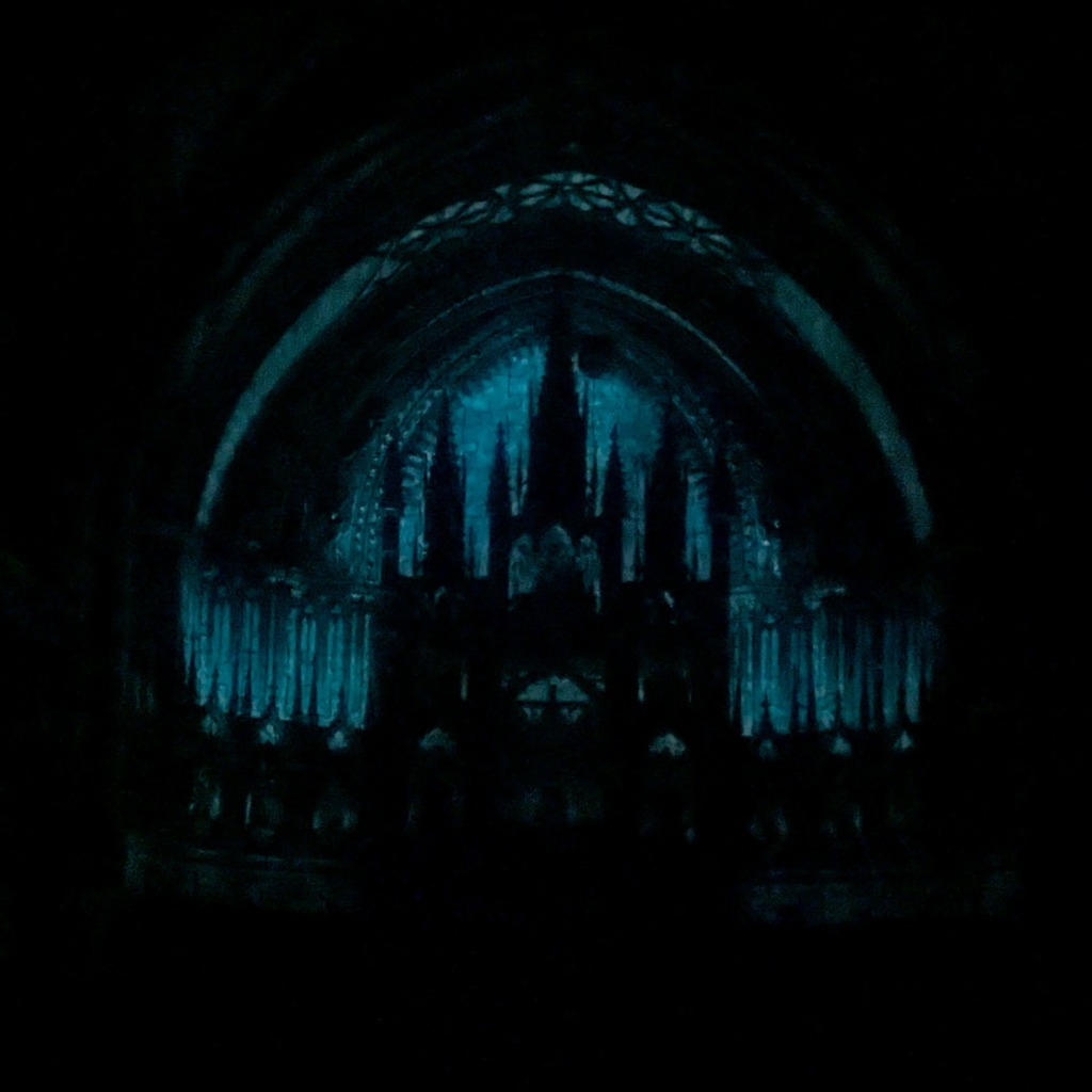 Glow-in-the-dark illustration of a silhouetted Gothic cathedral interior against a blue radiant background.