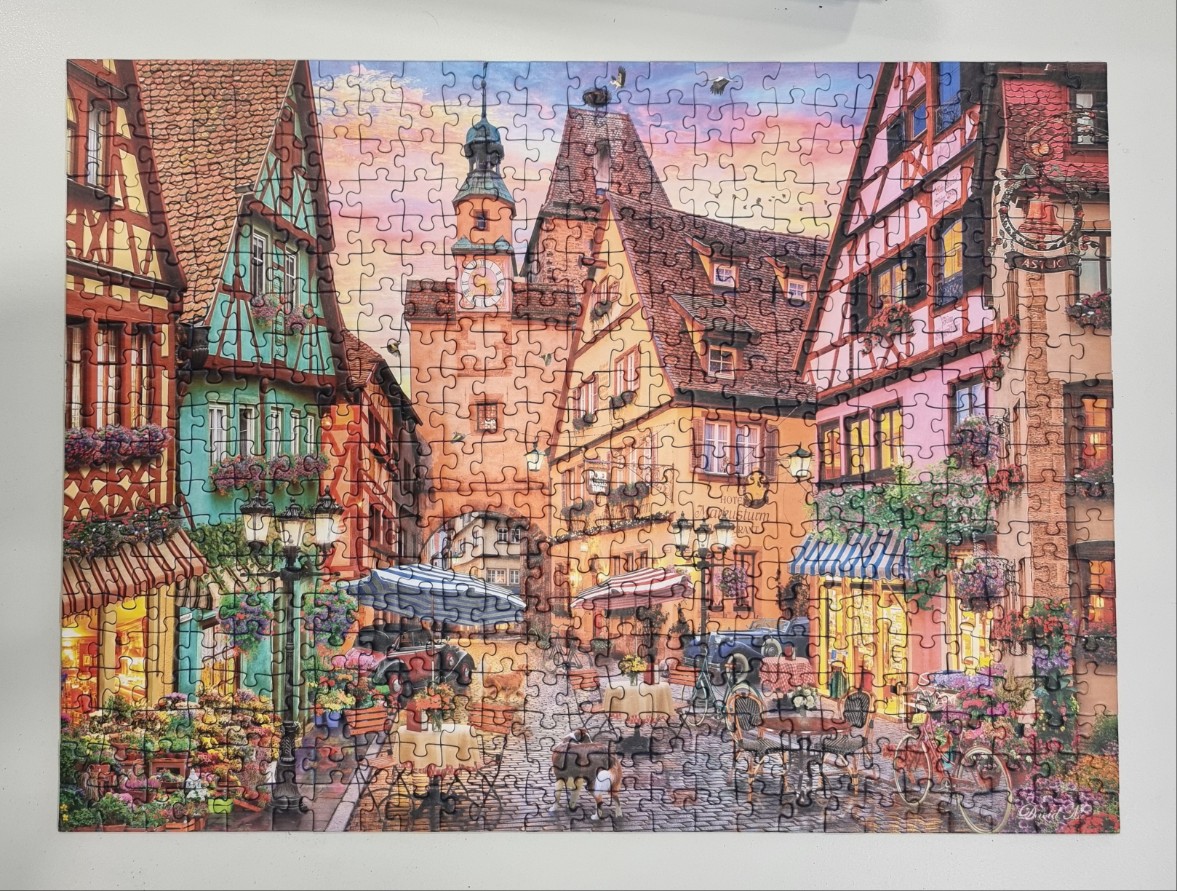 An illustration of a charming cobblestone town square with half-timbered buildings and outdoor dining at dusk.