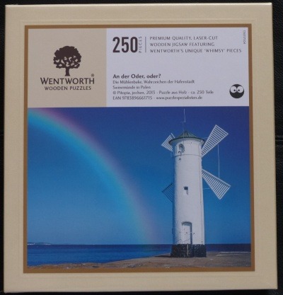 A white windmill beacon on a waterfront under a clear blue sky with a faint rainbow arching overhead.
