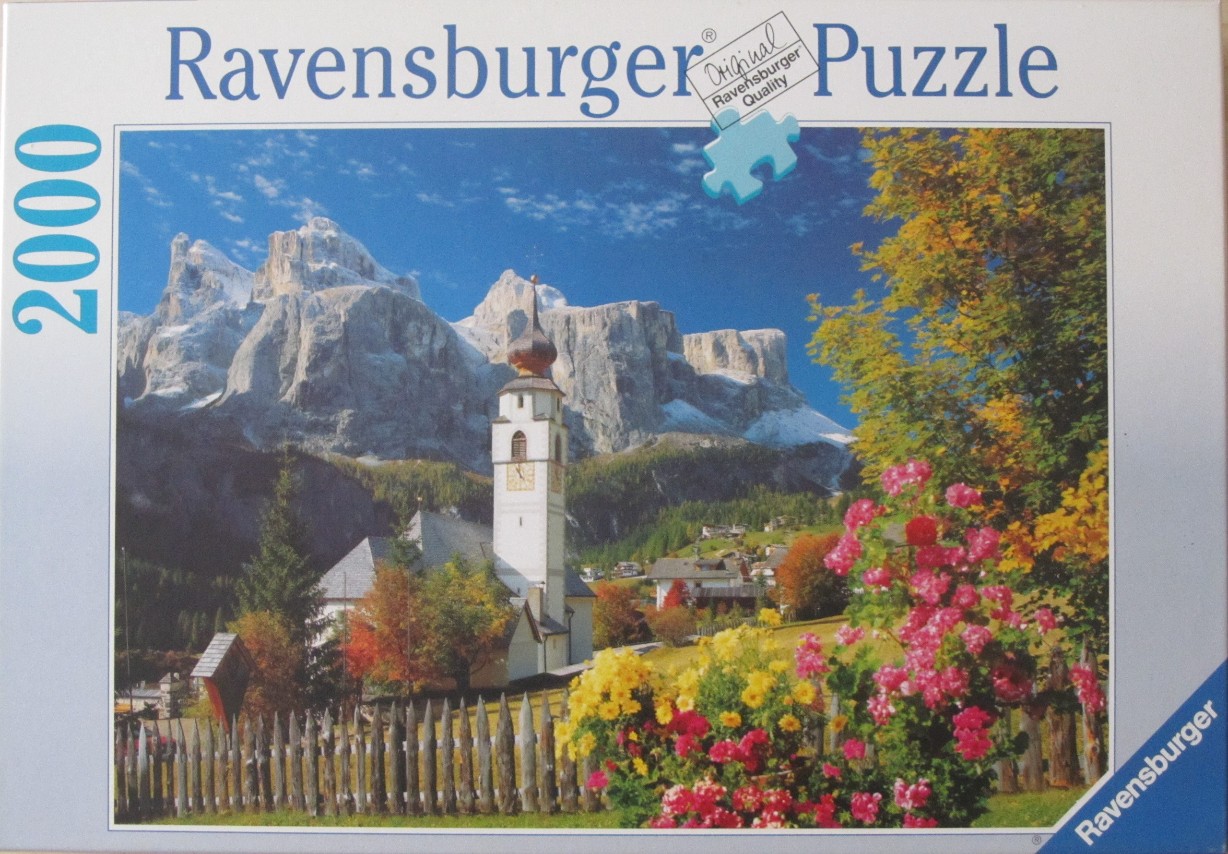 A village church in front of snowy Dolomite mountain peaks surrounded by autumn foliage and flowers.