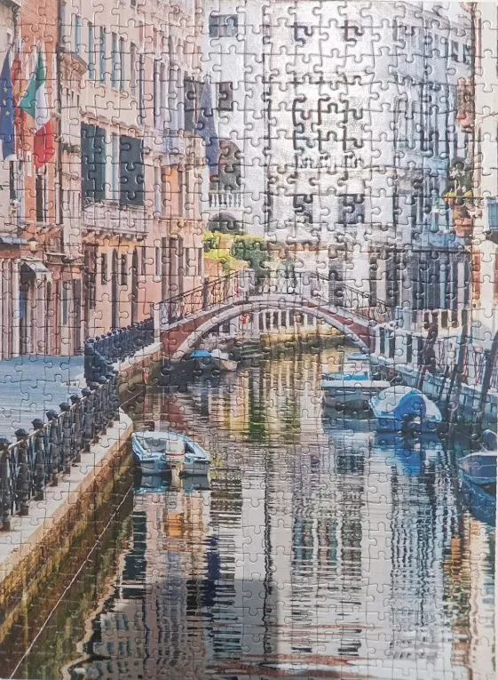 A peaceful canal scene in Venice featuring a stone bridge, historic buildings, and small motorboats.