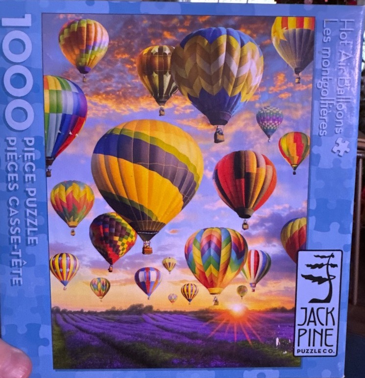 Many colorful hot air balloons floating above a purple lavender field at sunset