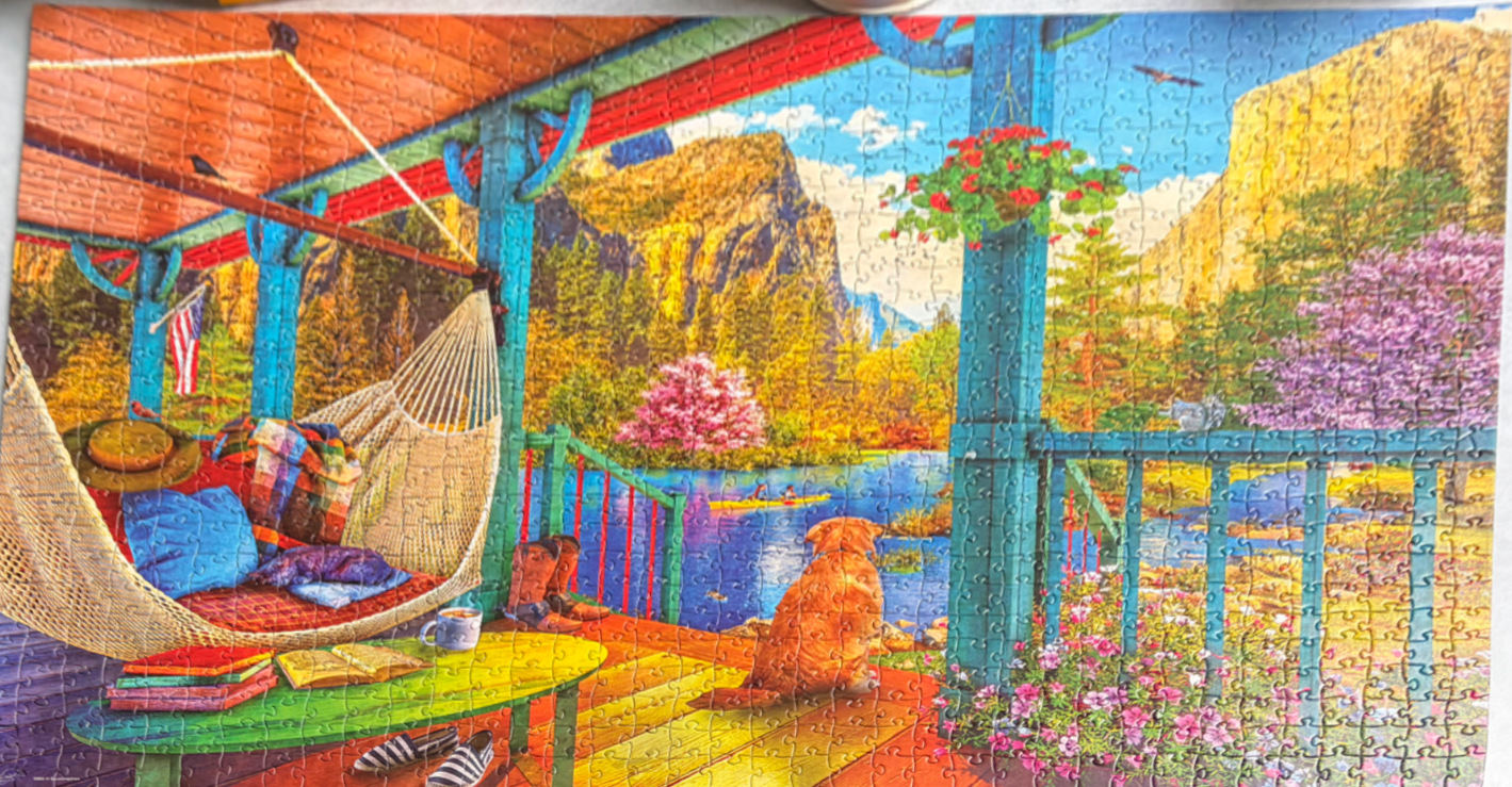 A peaceful porch overlooking a lake and mountains with a golden retriever sitting and a hammock nearby.