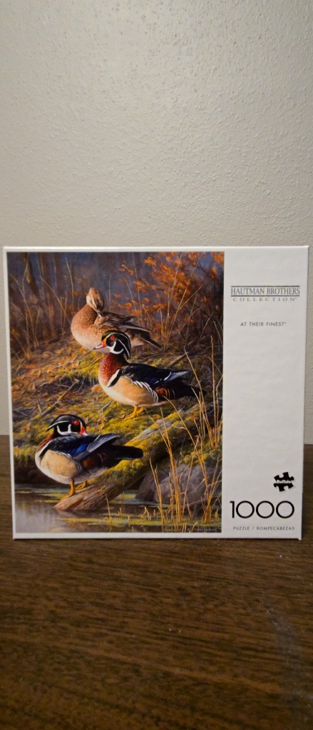 Three wood ducks perched on a mossy log by a pond in an autumn forest setting.