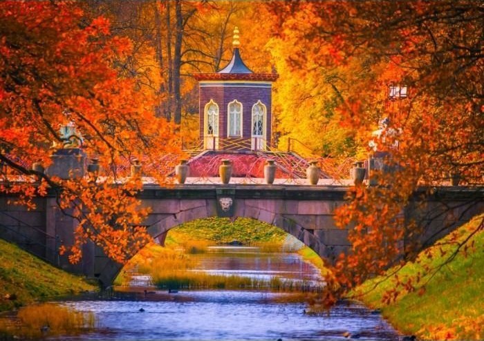 A stone bridge with a Chinese-style pavilion over a canal surrounded by vibrant autumn trees