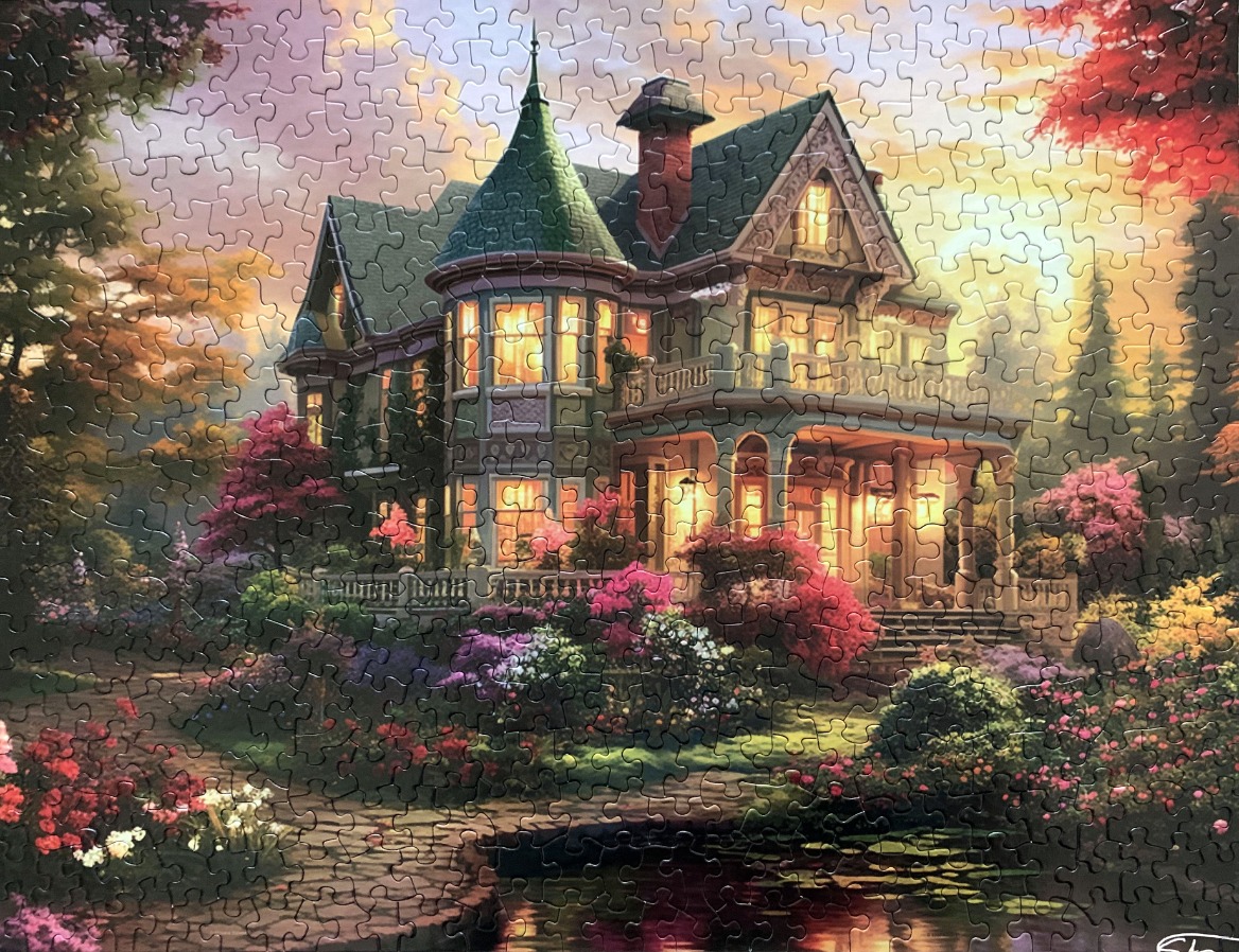 A Victorian house with a turret at sunset surrounded by lush gardens and a pond.