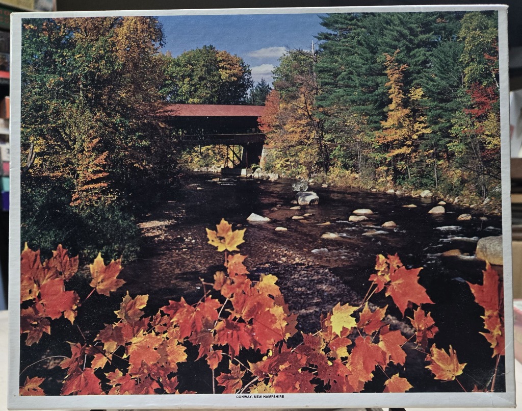 A covered wooden bridge over a stream in Conway, New Hampshire during autumn.