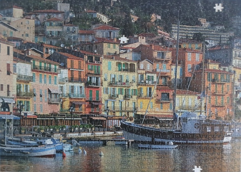 A Mediterranean harbor scene with colorful townhouses built into a hillside overlooking fishing boats in the water.