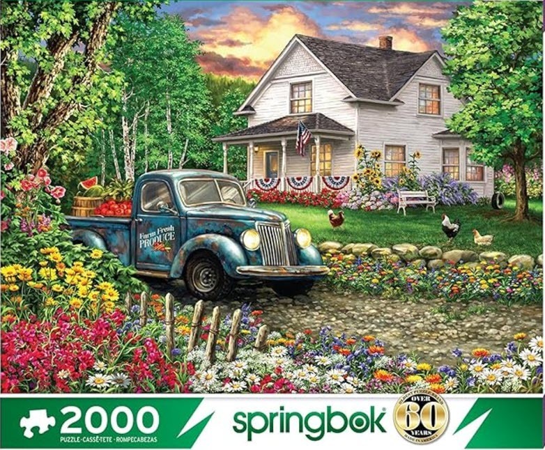 A vintage blue pickup truck filled with produce sits in front of a white farmhouse at sunset.