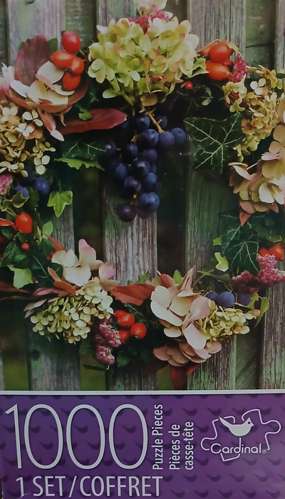 A lush autumn wreath featuring hydrangea, dark grapes, and bright orange berries hanging on a weathered wooden fence.