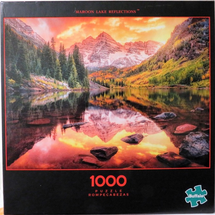 A scenic photograph of the Maroon Bells reflecting in Maroon Lake at sunset with vibrant orange and gold light.