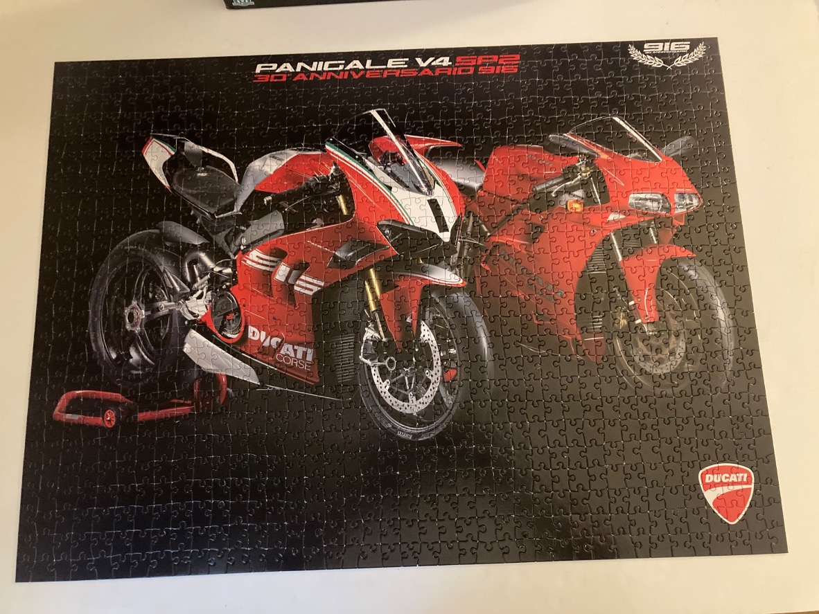 Two red Ducati motorcycles, a modern Panigale V4 SP2 and a classic 916, against a black background.