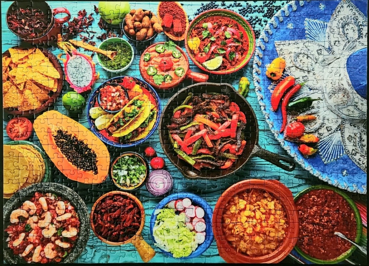 A flat-lay photograph of a festive Mexican feast featuring tacos, fajitas, salsas, and a large blue sombrero.