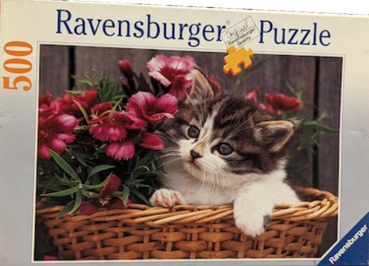 A fluffy tabby kitten peeking out from a wicker basket filled with pink carnations.
