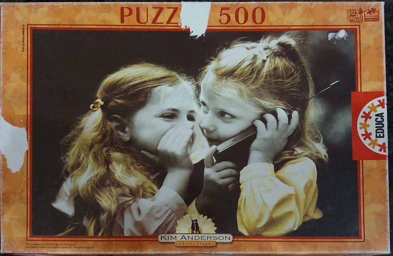 Two young girls with blonde hair sharing a secret while one holds a vintage mobile phone.