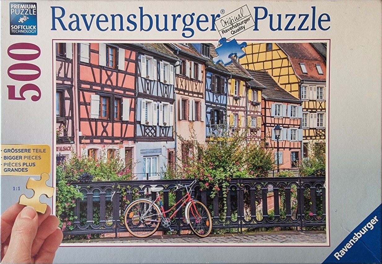 A row of colorful half-timbered houses in Alsace, France, with a bicycle parked against a wrought-iron fence.