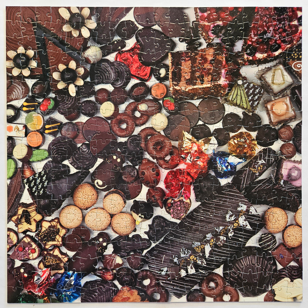An overhead view of a dense, cluttered arrangement of assorted chocolates, cookies, and small cakes.