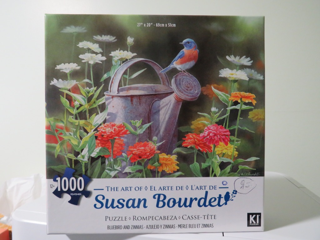 A bluebird perched on a watering can surrounded by colorful zinnias.