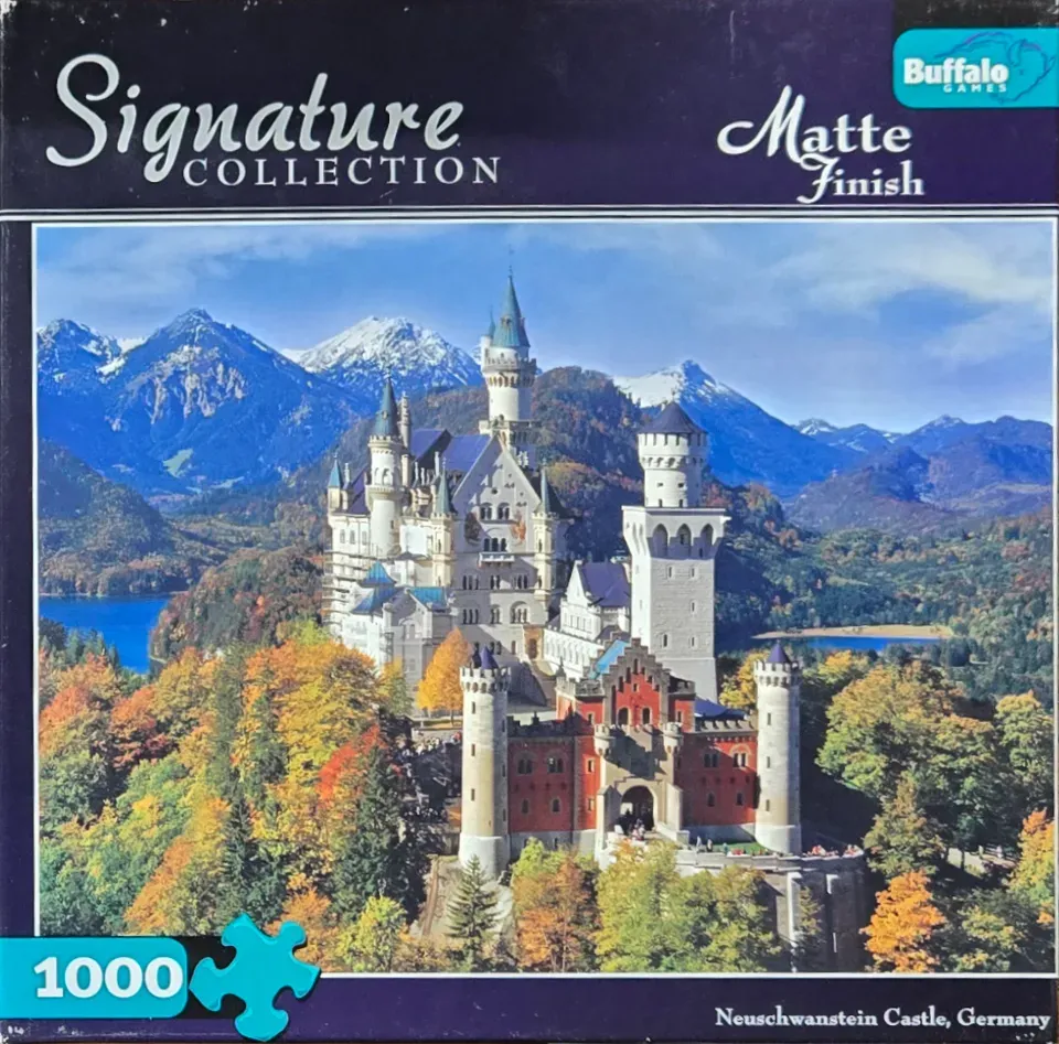 Neuschwanstein Castle surrounded by autumn forest and snow-capped mountains.