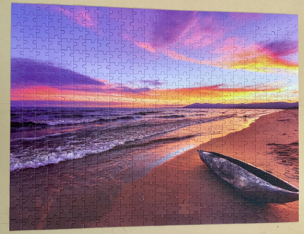 A weathered wooden boat resting on a sandy beach at sunset with a vibrant purple and orange sky.