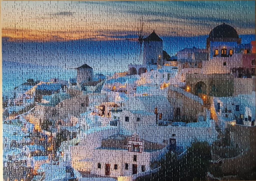 A panoramic view of the whitewashed buildings and blue-domed churches of Oia, Santorini at dusk.