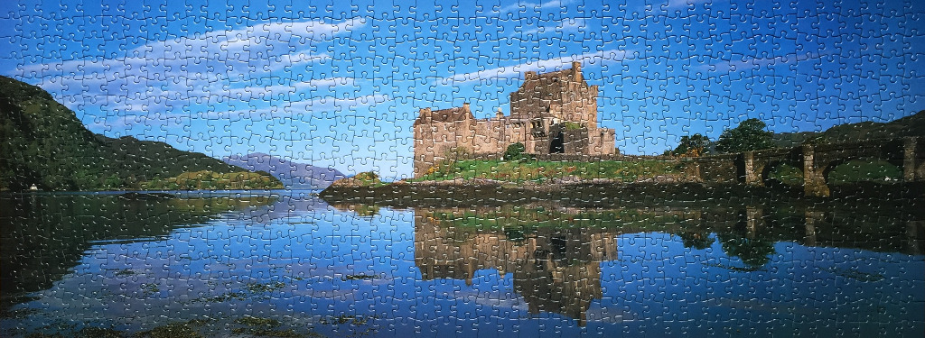 A panoramic photograph of Eilean Donan Castle in Scotland reflected in the calm waters of the loch.