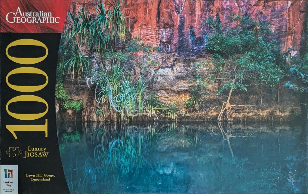 A photograph of the calm, turquoise waters of Lawn Hill Gorge reflecting the red rocky cliffs and green pandanus plants.