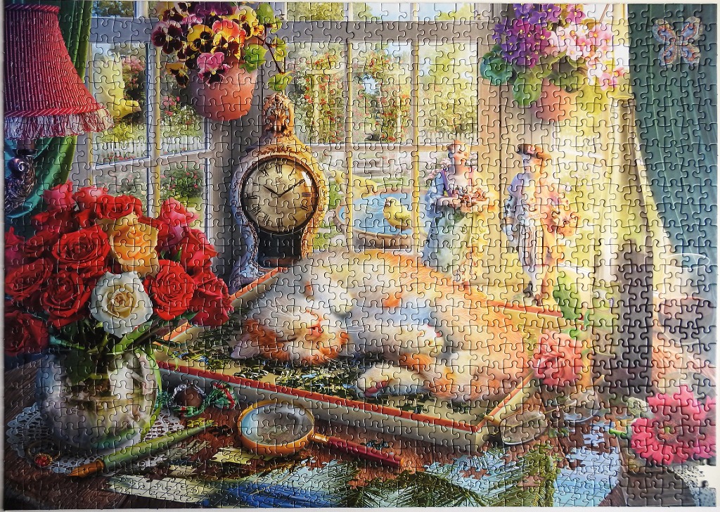 A ginger cat sleeps on a desk in a sunny room filled with roses, a clock, and a window view of a garden.