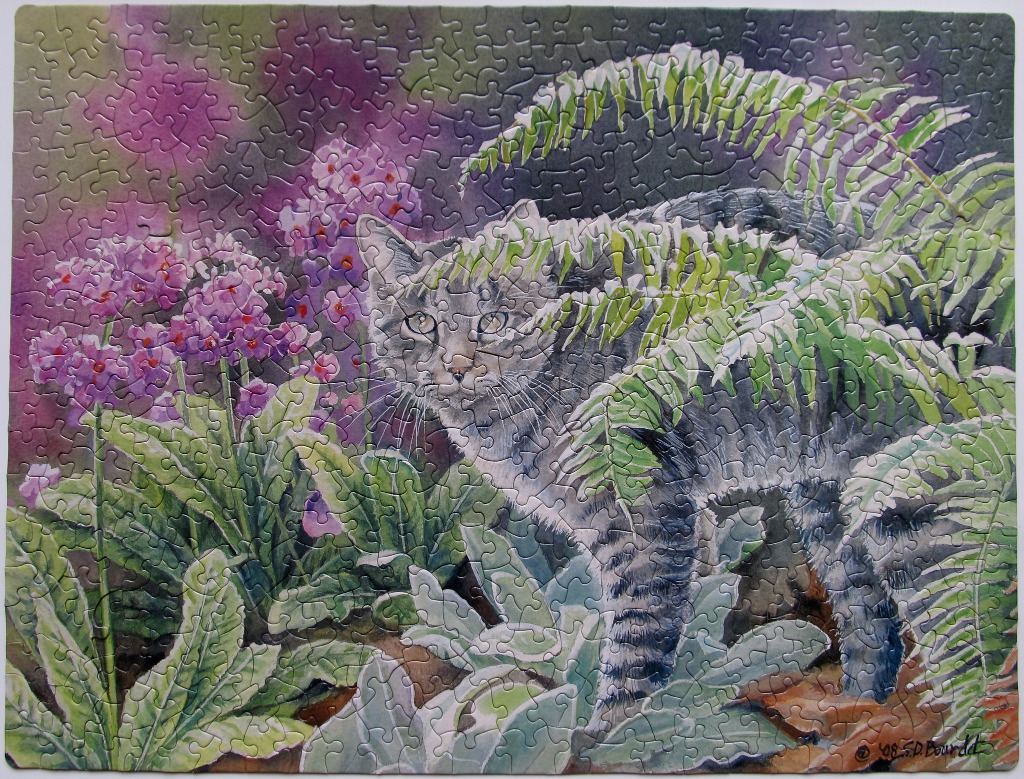 A grey tabby cat partially hidden by lush ferns and purple flowers in a garden setting.