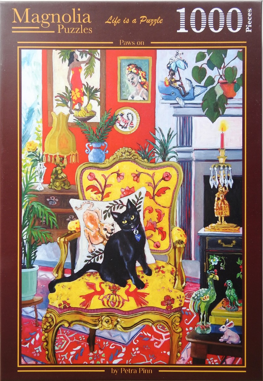 A black cat sits on a yellow ornate chair in a vibrantly decorated room full of art and plants.