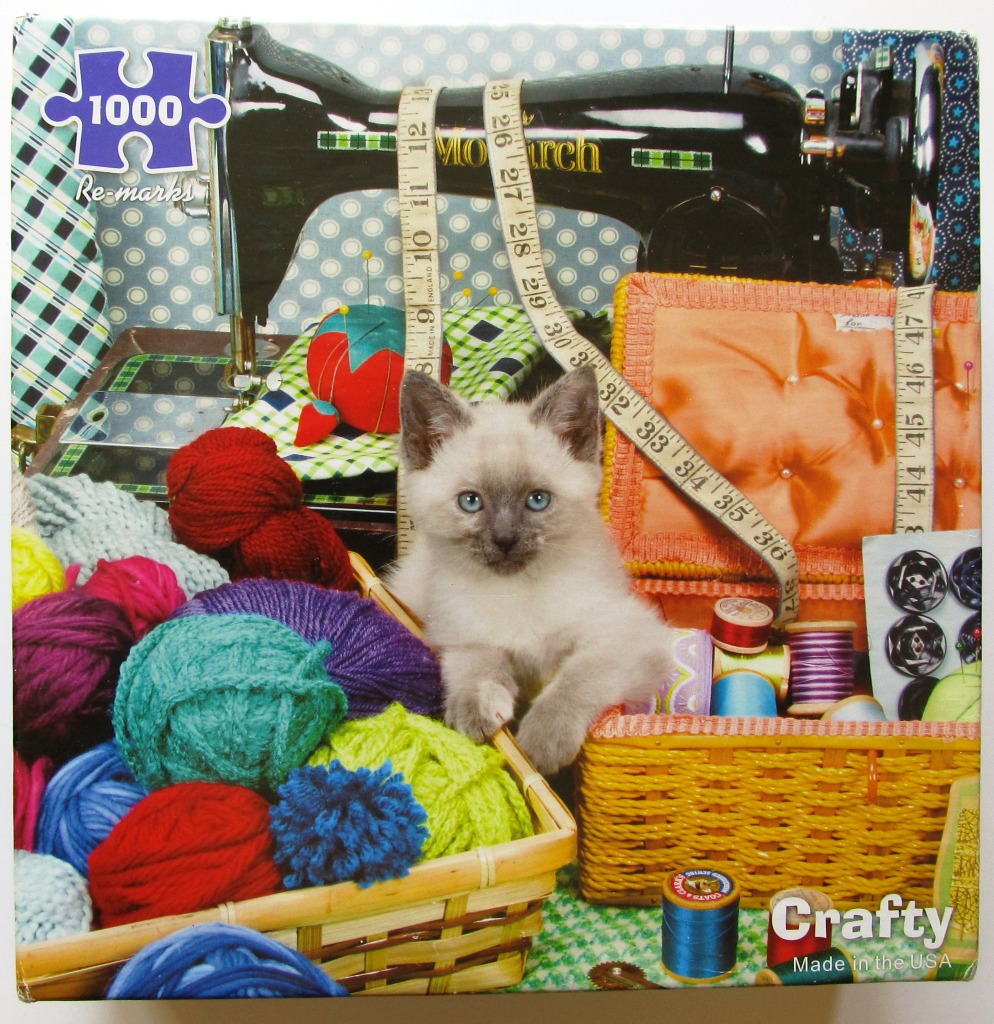 A Siamese kitten sits among baskets of colorful yarn and sewing supplies in front of a vintage sewing machine.