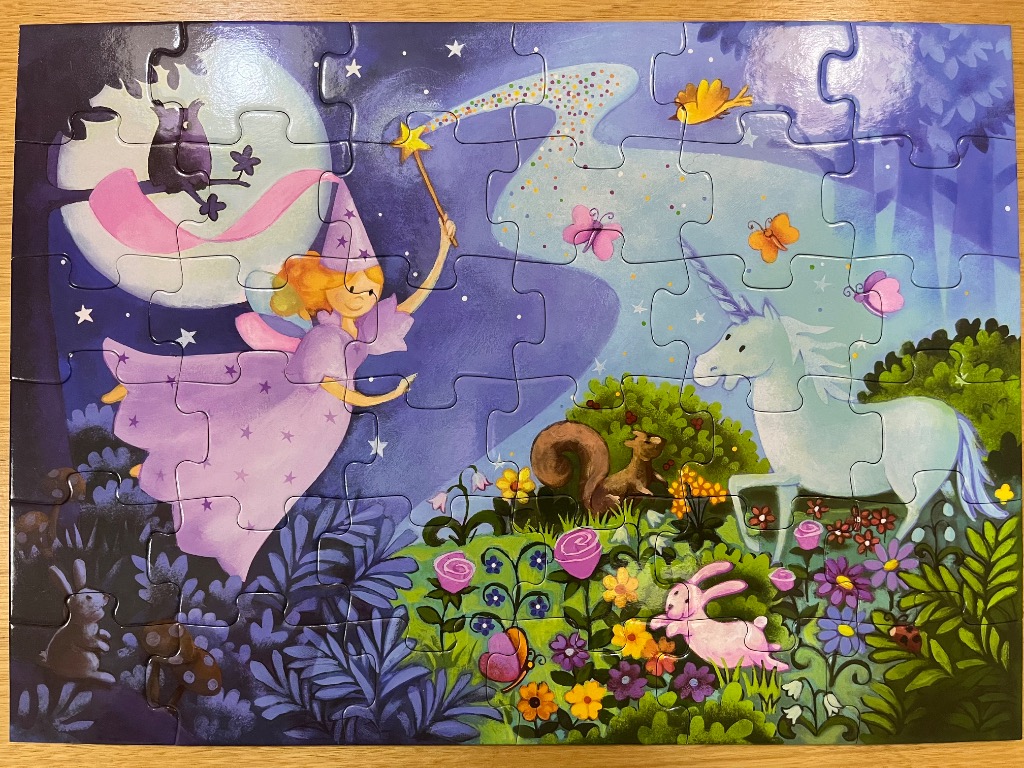 A whimsical illustration of a fairy waving a magic wand over a unicorn and woodland creatures in a magical forest at night.