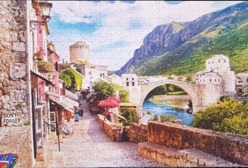 A scenic view of the Stari Most bridge in Mostar, Bosnia and Herzegovina, with a cobblestone street and stone buildings.