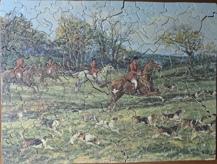 A traditional fox hunting scene featuring riders on horseback and a pack of hounds running through a meadow.